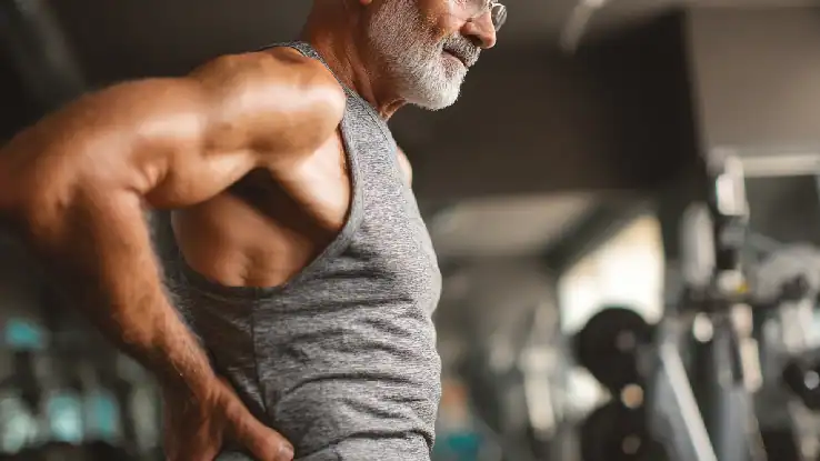Older man experiencing back pain after workout at gym.